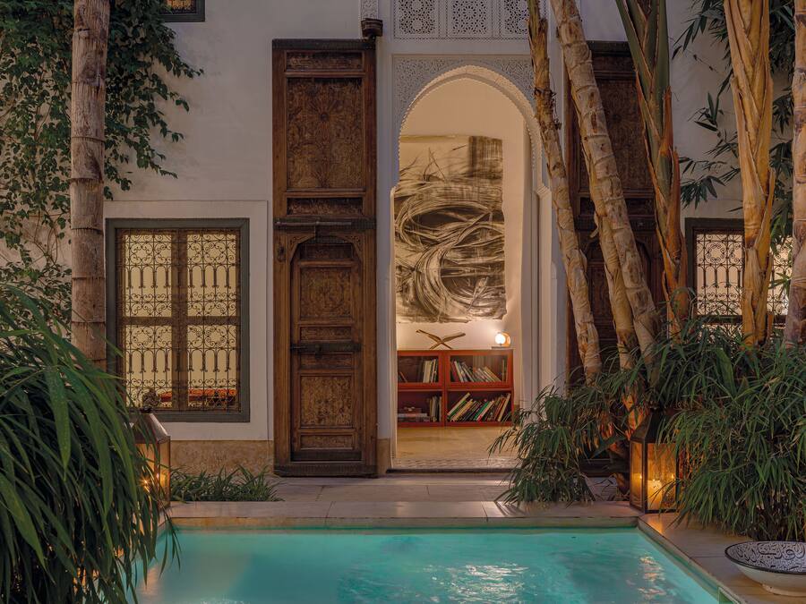 A pool area with a wooden door, bookshelves, and a large arched doorway.