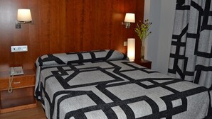 A hotel room with a wooden headboard, two bedside lamps, a telephone, a vase with flowers, and a patterned bedspread. - Hotel Jarama (Zamora)
