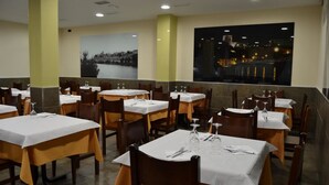 A restaurant with multiple tables set for dining, featuring a view of a cityscape at night. - Hotel Jarama (Zamora)