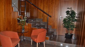 A modern lobby with a staircase, two orange chairs, a small table with a vase, and a potted plant. - Hotel Jarama (Zamora)