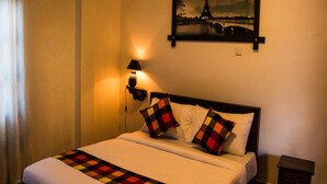 Una habitación de hotel con cama, mesita de noche, lámpara y un cuadro de la Torre Eiffel.