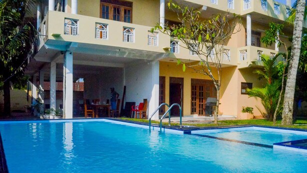 Una piscina con superficie de agua azul transparente, rodeada por un área exterior cubierta y un edificio al fondo.