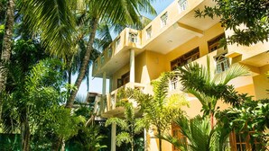 Un edificio de varios pisos con balcones, rodeado de exuberante vegetación tropical.
