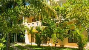 Un edificio con fachada amarilla, rodeado de exuberante vegetación y palmeras.