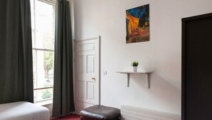 A room with a bed, a window with curtains, a door, a radiator, and a small shelf with a plant. - Metrostays - O'Connell Street 84-1 (Dublin)