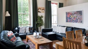 A living room with two black leather sofas, a wooden coffee table, and a dining table with chairs. There is a potted plant, a chandelier, and artwork on the walls. - Metrostays - O'Connell Street 84-1 (Dublin)