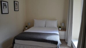 Un cuarto de hotel ordenado, con una cama grande, dos mesitas de noche y una ventana con cortinas.