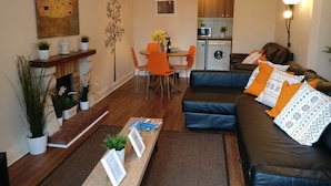 Una sala moderna con un sofá, una mesa de comedor y sillas. Hay una zona de cocina con lavadora y microondas.