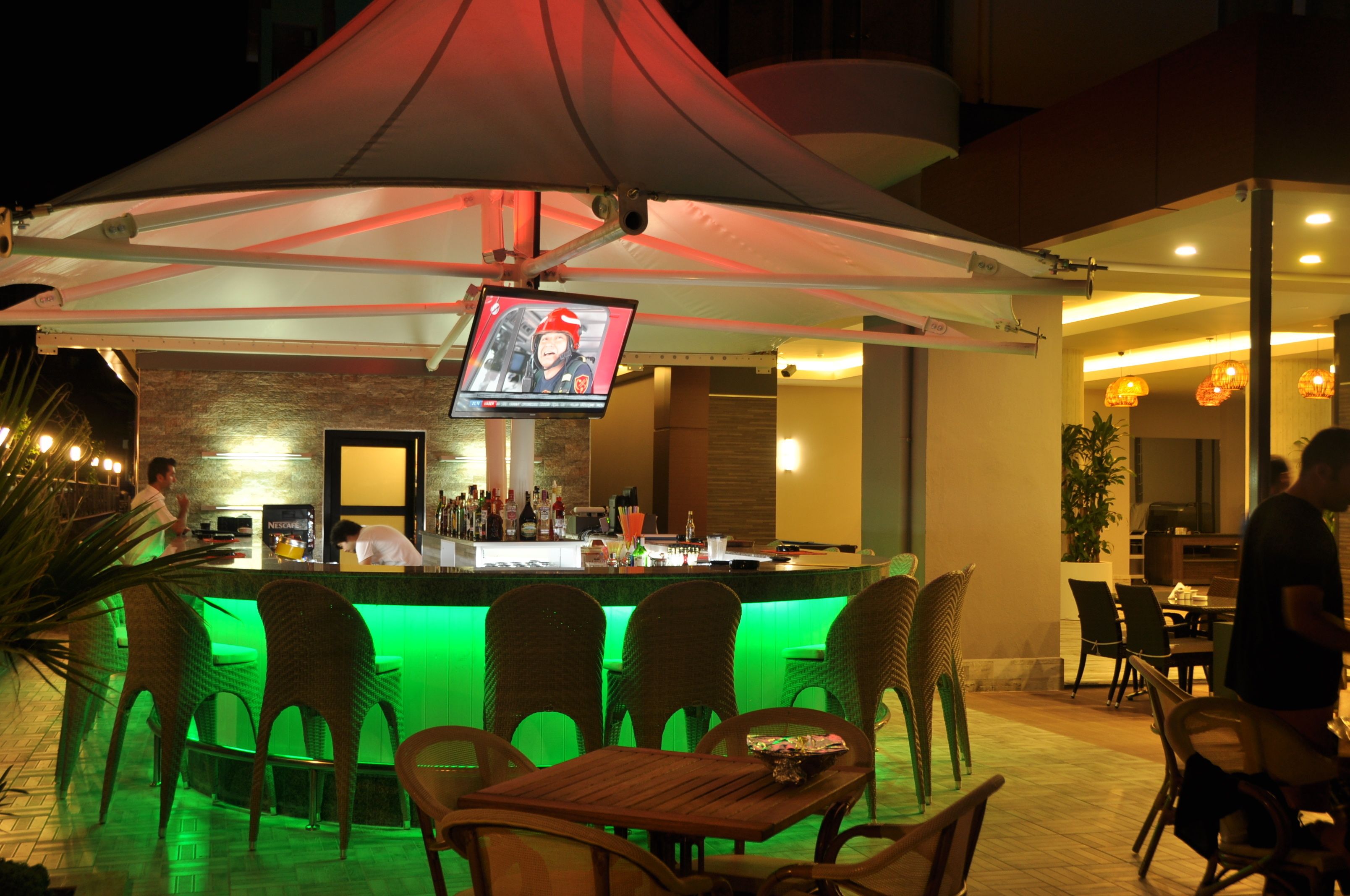 An outdoor bar area with a counter, chairs, and a television screen.