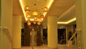 A hotel lobby with a modern design, featuring a central staircase, multiple hanging spherical lights, and a view into the dining area. - Vega Green Apart Hotel (Alanya)