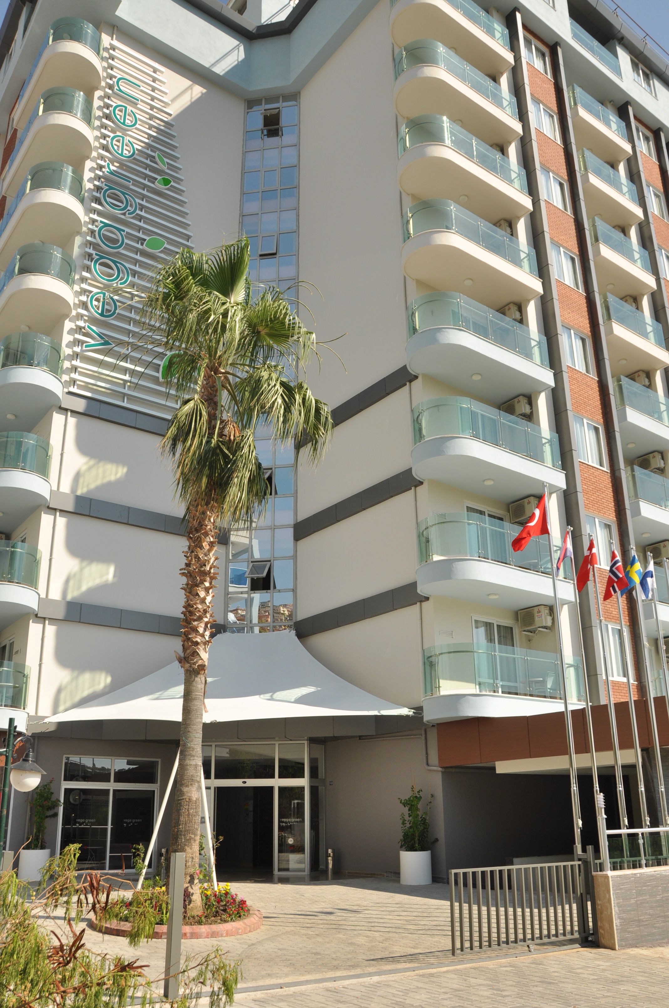 A modern hotel with multiple balconies, a palm tree, and flags.
