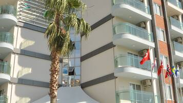 A modern hotel with multiple balconies, a palm tree, and flags.
