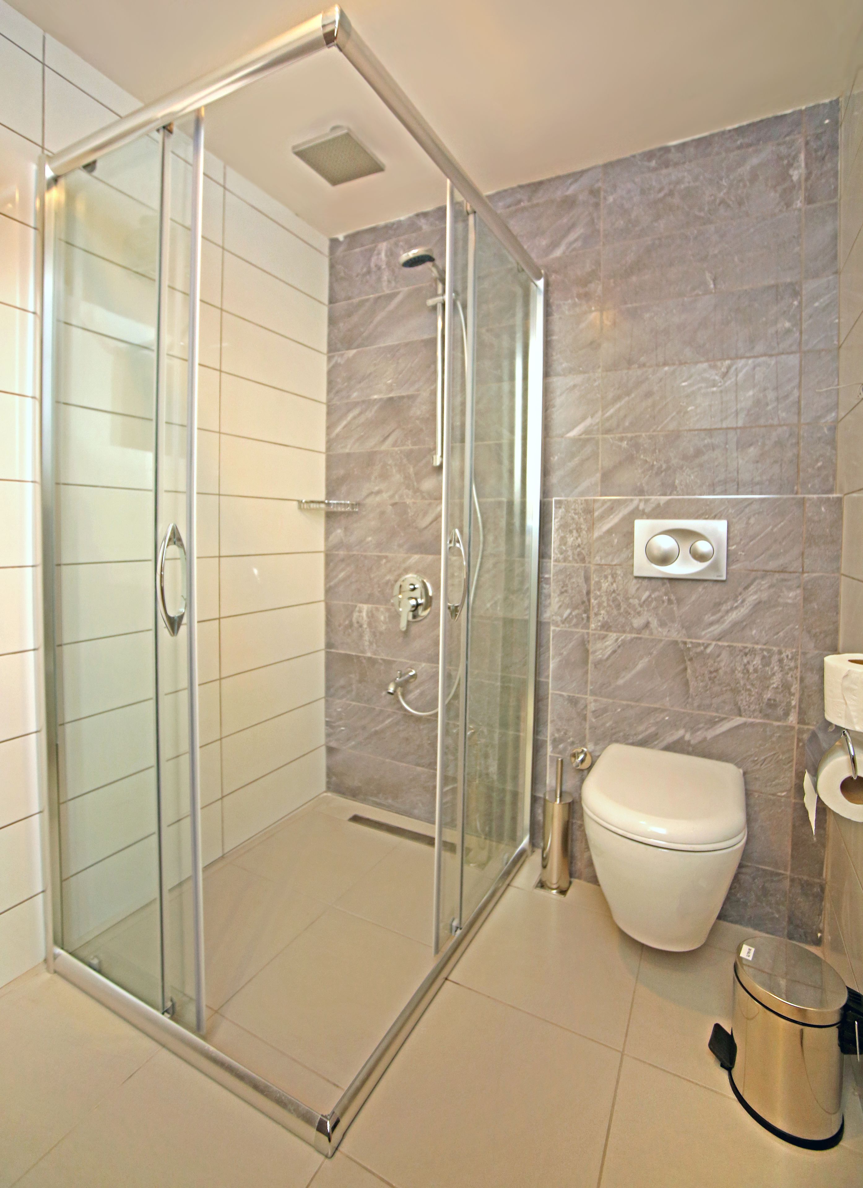 Un baño moderno con ducha de vidrio, inodoro y cubo de basura.