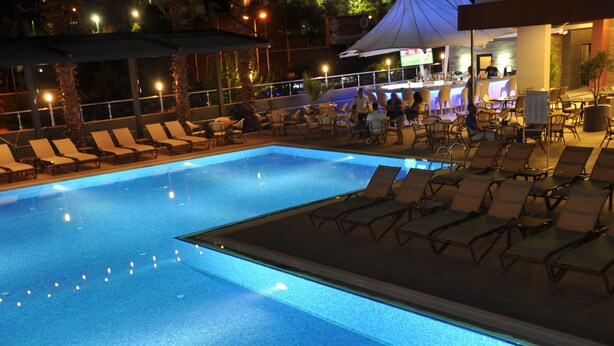 A swimming pool with lounge chairs and umbrellas, surrounded by a bar and seating area. - Vega Green Apart Hotel (Alanya)