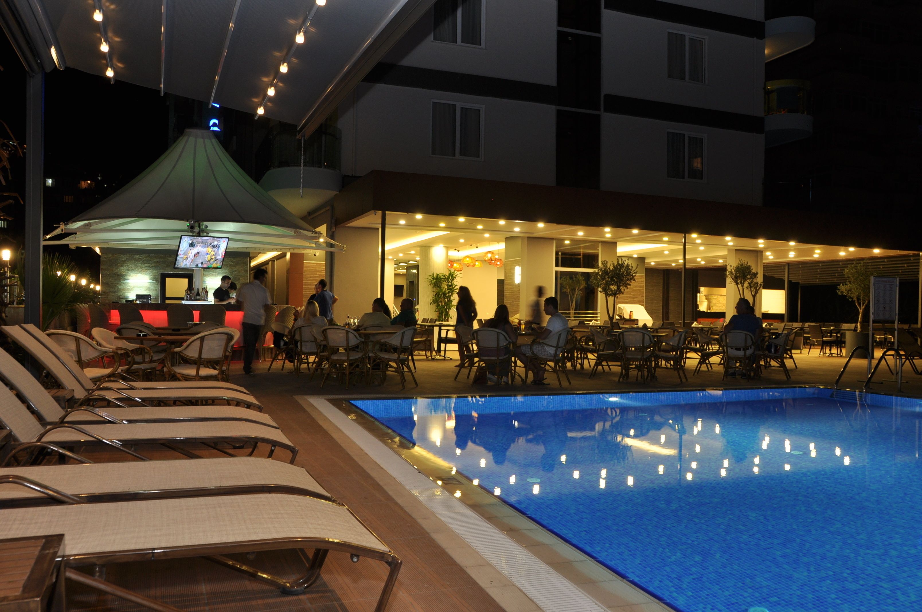 Un espace aménagé au bord de la piscine, avec des chaises longues, un bar et des tables sous une zone abritée.