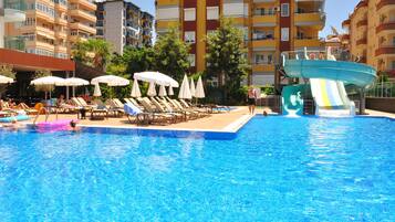 A swimming pool with lounge chairs and umbrellas, surrounded by multi-story buildings.