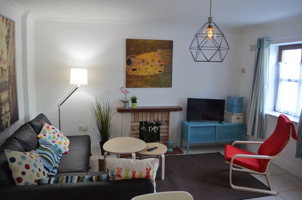 A living room with a sofa, a red chair, a fireplace, a television, and a painting on the wall.