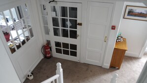 Un pasillo con una puerta blanca, una pequeña mesa de madera y un extintor.