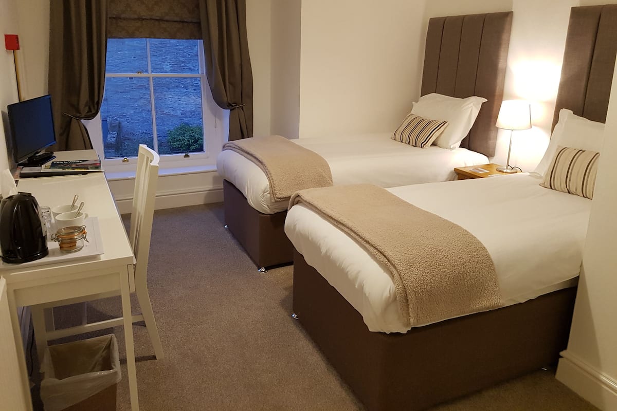 Habitación de hotel con dos camas, un escritorio con computadora, una silla, ventana con cortinas y vista al exterior.