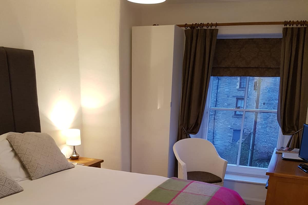 Habitación de hotel con cama, una silla, escritorio, lámpara y ventana con cortinas.