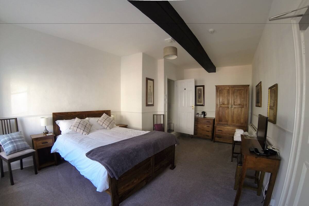 Ein Schlafzimmer mit einem Bett, Nachttischen, einem Schreibtisch mit Stuhl, einem Kleiderschrank und einem Fernseher.