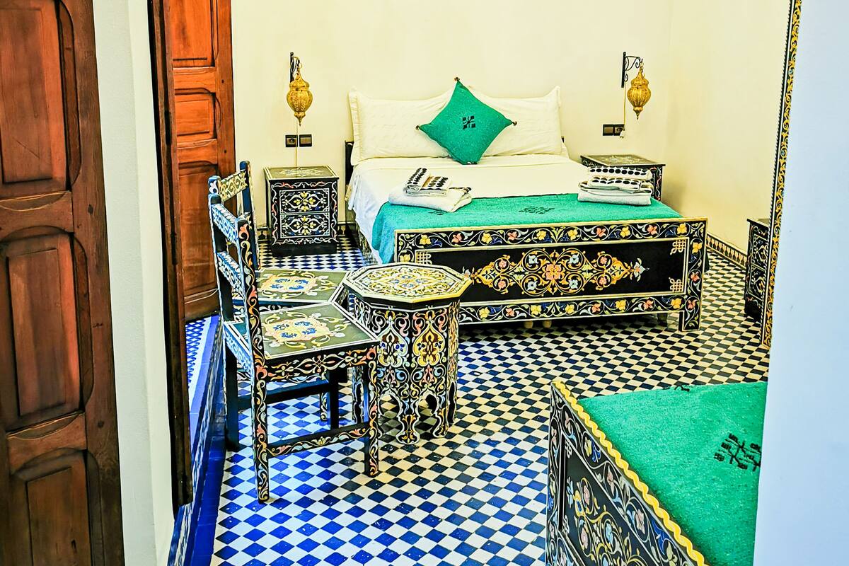 Una habitación con piso a cuadros, una cama con almohada verde, una lámpara de araña y una puerta de madera.
