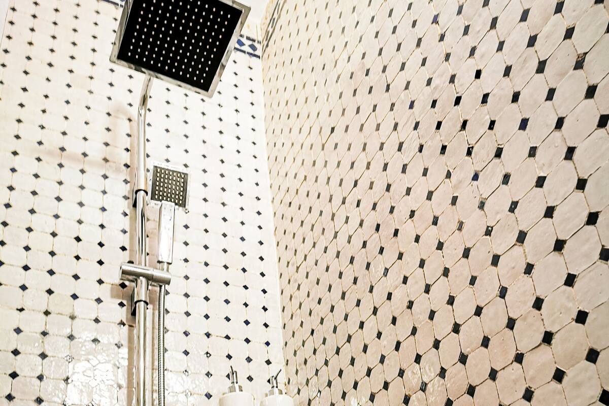 Un baño con pared de azulejos que presenta un diseño geométrico, un cabezal de ducha y dos porta papel higiénico.