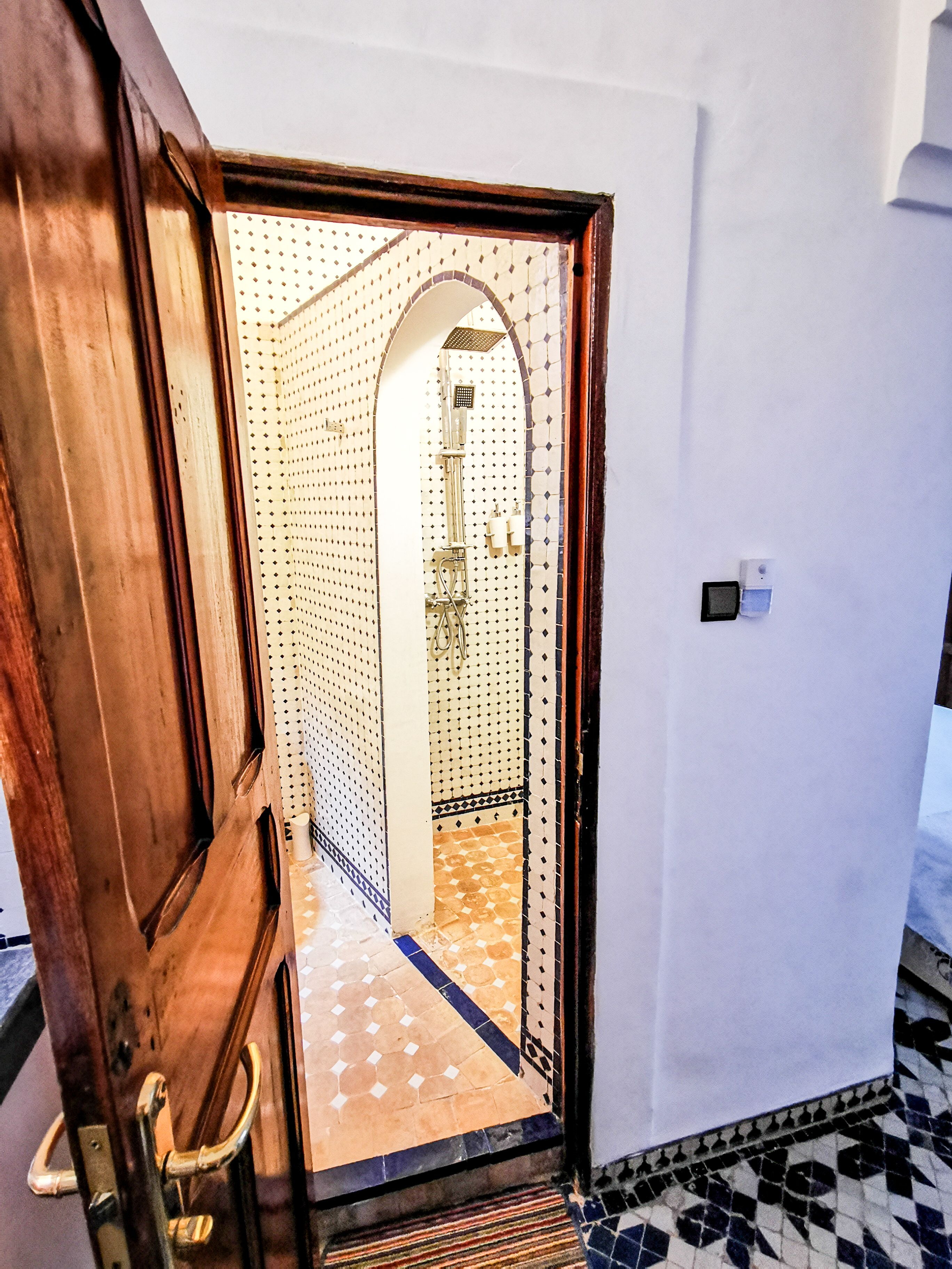 Een houten deur die leidt naar een badkamer met een betegelde vloer en een douchehoek.