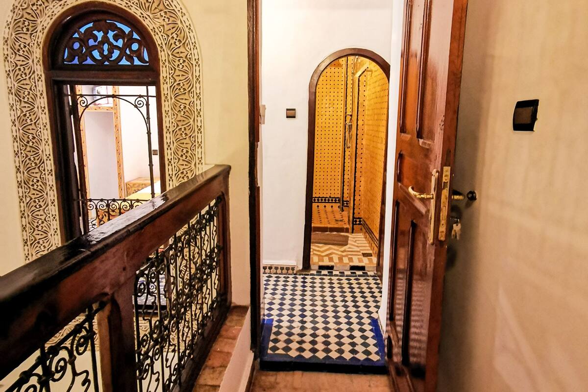 Un pasillo con puertas de madera ornamentadas, piso estampado y barandilla decorativa.