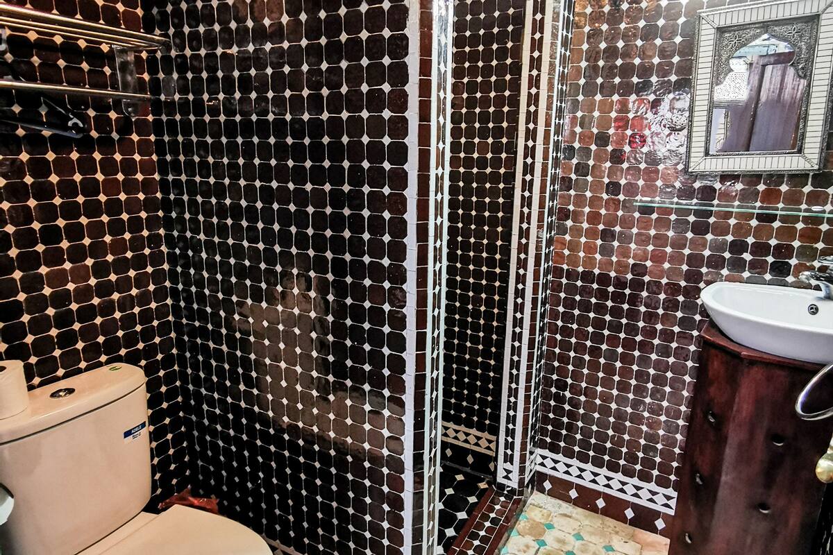 Baño con inodoro, ducha, lavabo y paredes con azulejos.