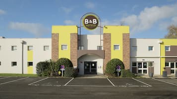 A B&B hotel with a yellow and white facade, a central entrance, and a parking lot.