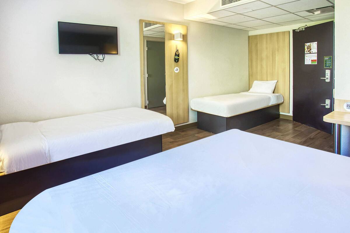 A hotel room with two single beds, a TV mounted on the wall, and a wooden door.