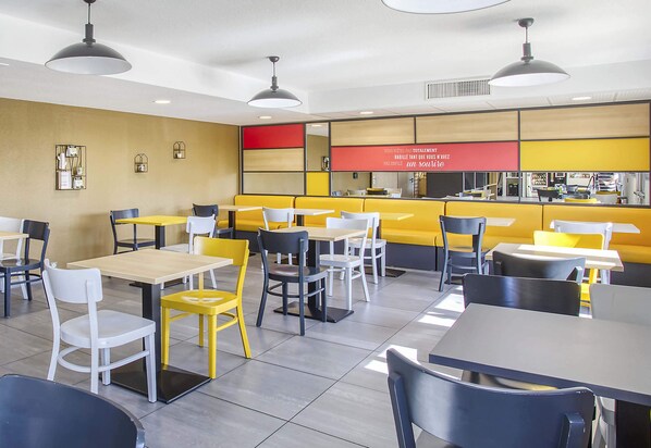 Un interior de cafetería moderno con asientos amarillos y blancos, sillas negras y blancas, e iluminación colgante.