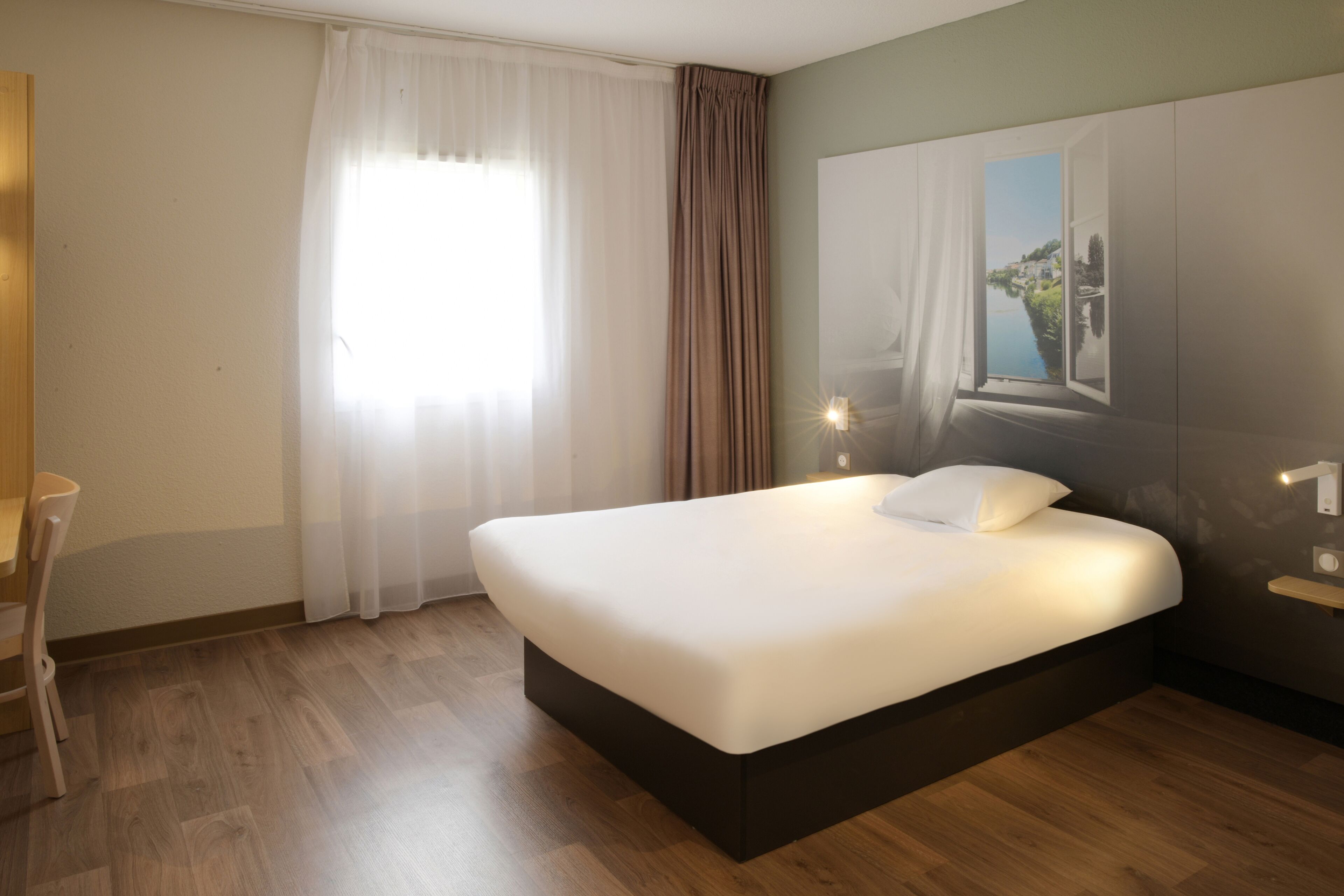 A modern hotel room with a large bed, a desk, and a view of a coastal landscape through a window.