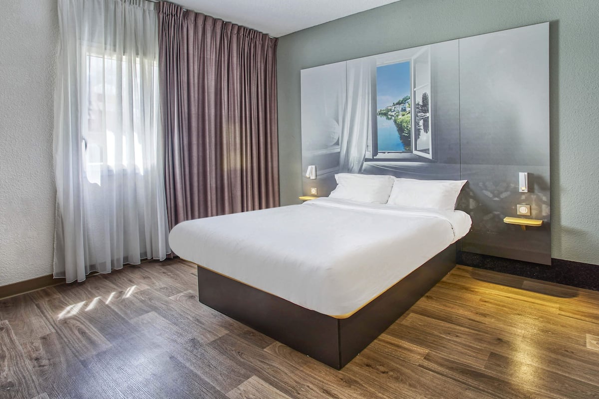 A modern hotel room with a large bed, a view of a coastal landscape through the window, and a minimalist design.