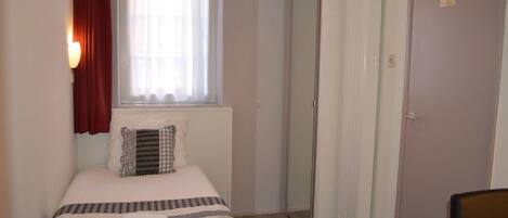 A small, neatly arranged bedroom with a bed, a bedside table, a mirror, and a wardrobe.