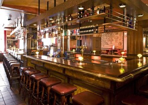 Un bar avec un long comptoir, des tabourets et des étagères remplies de bouteilles.