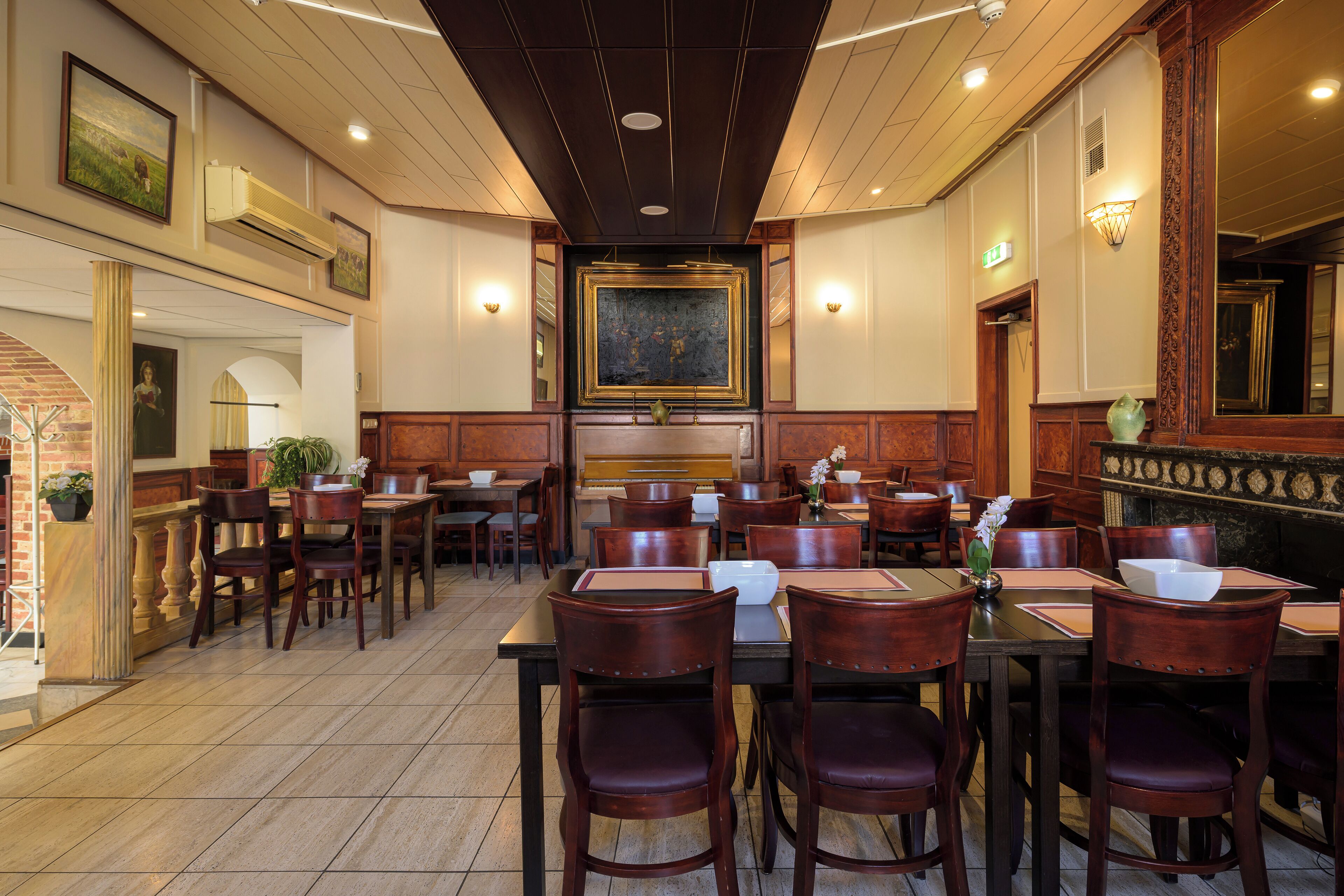 A restaurant with wooden tables and chairs, a central buffet area, and framed artwork on the walls.