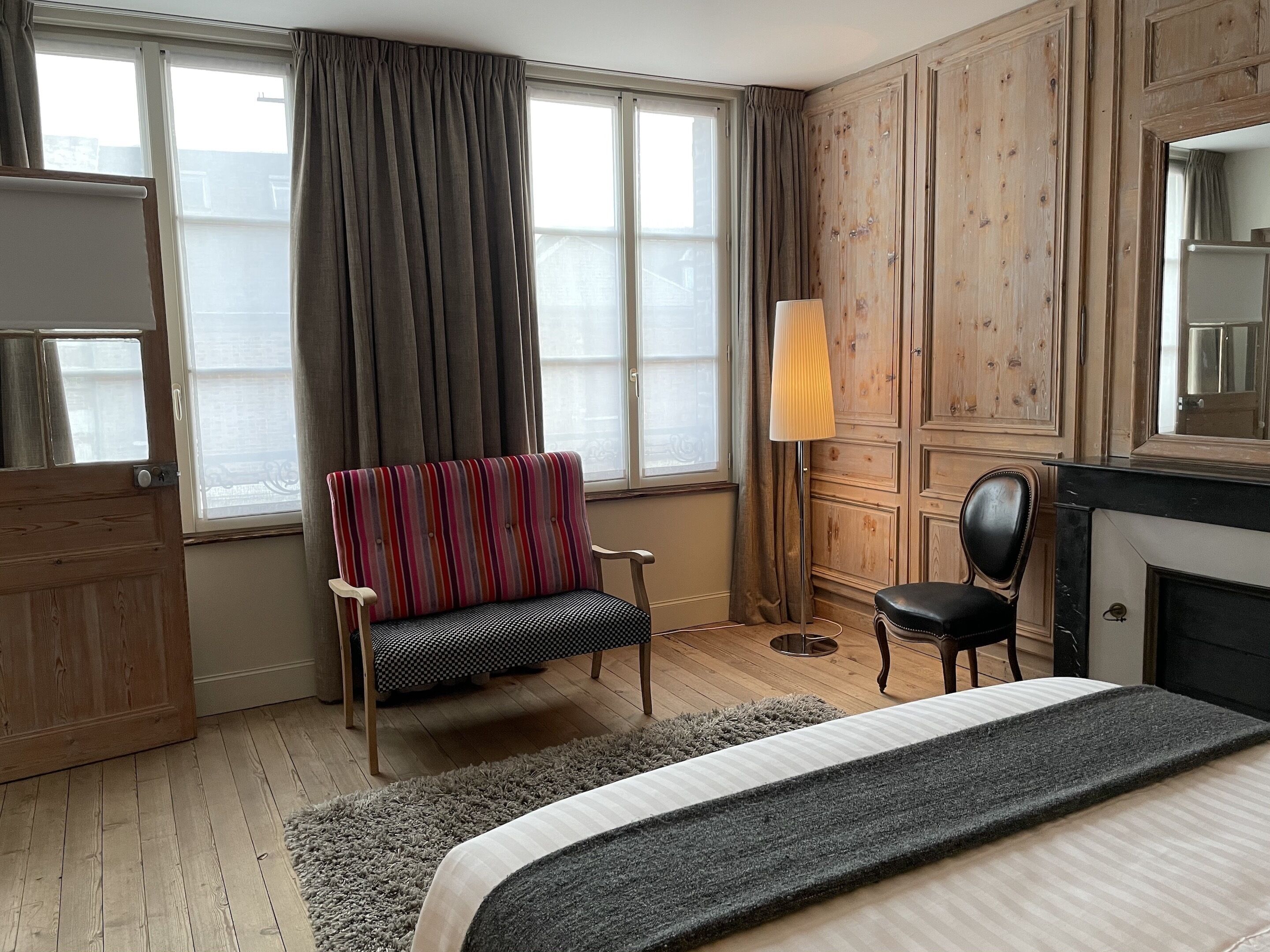 Ein Hotelzimmer mit einem Bett, einem gestreiften Sessel, einem kleinen Tisch, einer Lampe und einem Holzschrank.