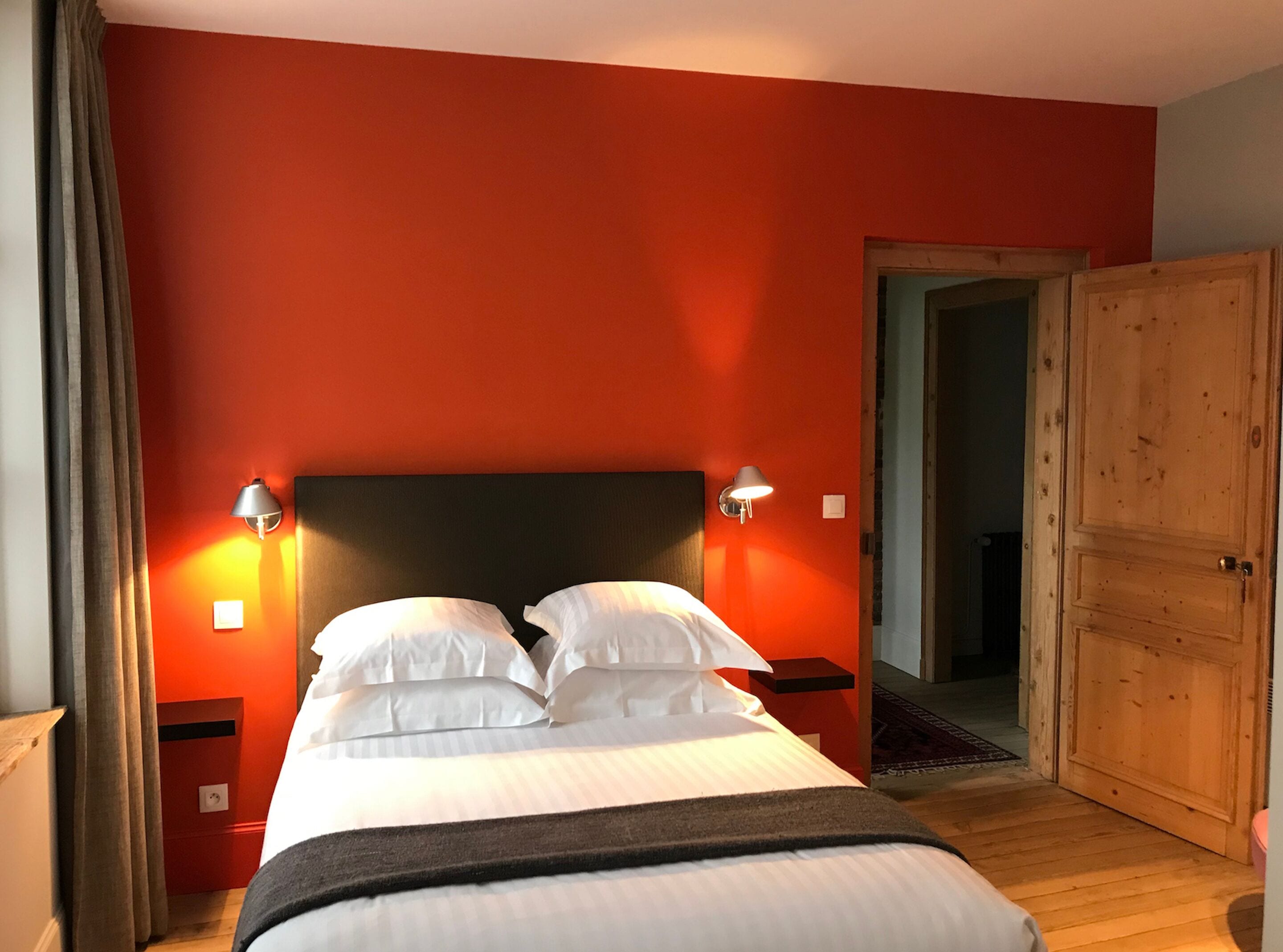 Une chambre d’hôtel avec un lit, deux lampes de chevet, une armoire en bois et un mur rouge.