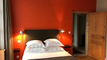 Une chambre d’hôtel avec un lit, deux lampes de chevet, une armoire en bois et un mur rouge.