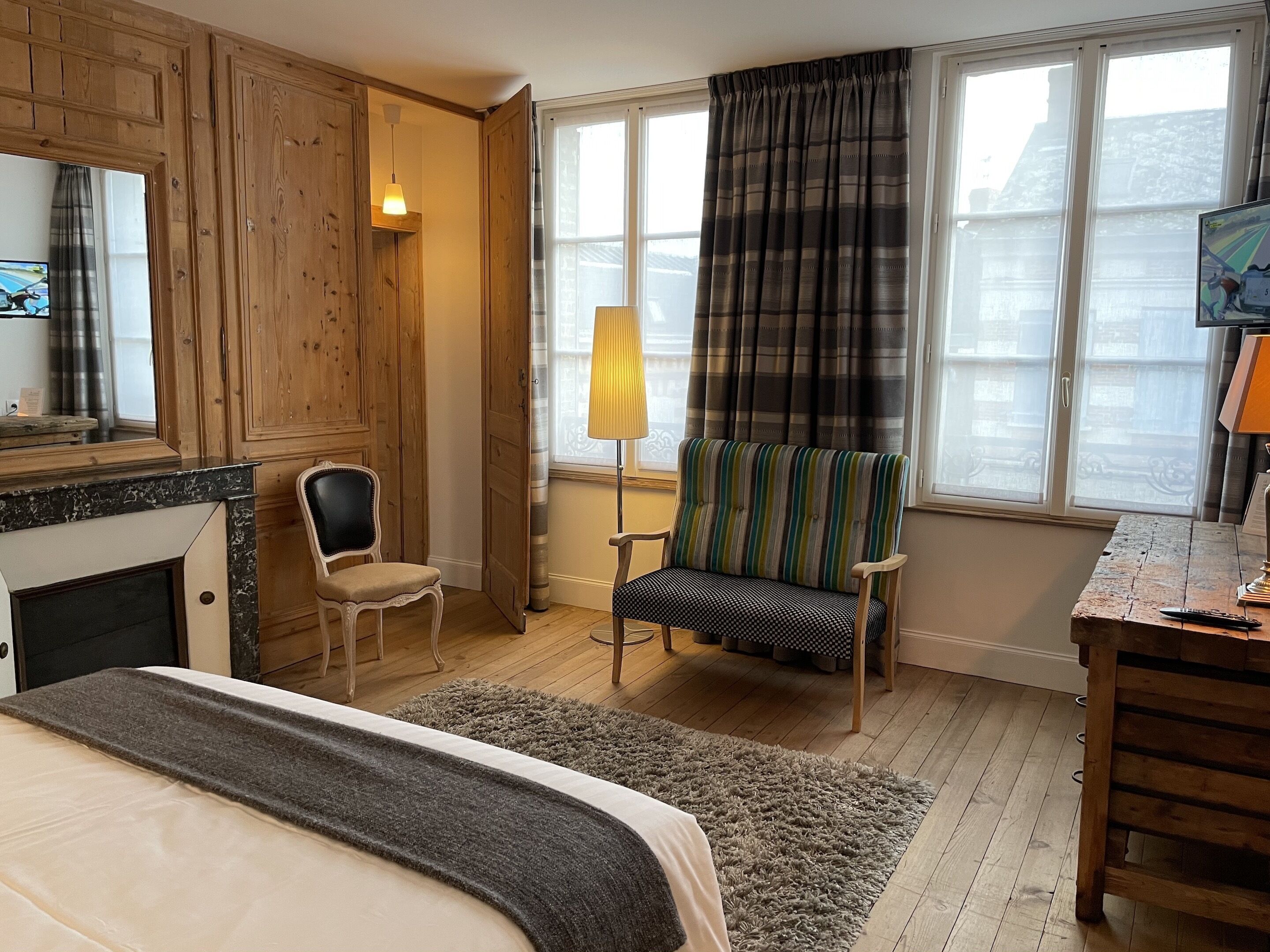 A hotel room with a bed, two chairs, a desk, a lamp, and a window with curtains.