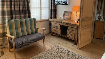 A cozy room with a striped chair, a wooden desk with drawers, a television mounted on the wall, and a large wooden door.