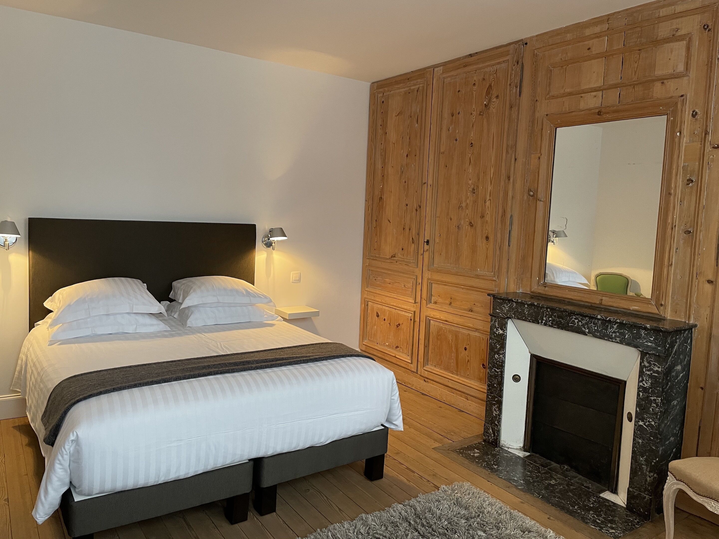 A bedroom with a bed, wooden panel walls, a fireplace, and a mirror.