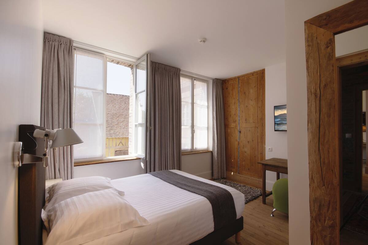 A hotel room with a bed, a desk, a chair, and a wooden wardrobe.
