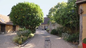 A gravel pathway leading to a building with a sloped roof, surrounded by greenery and a rooster decoration. - Le Jardin Découverte (Conches-en-Ouche)