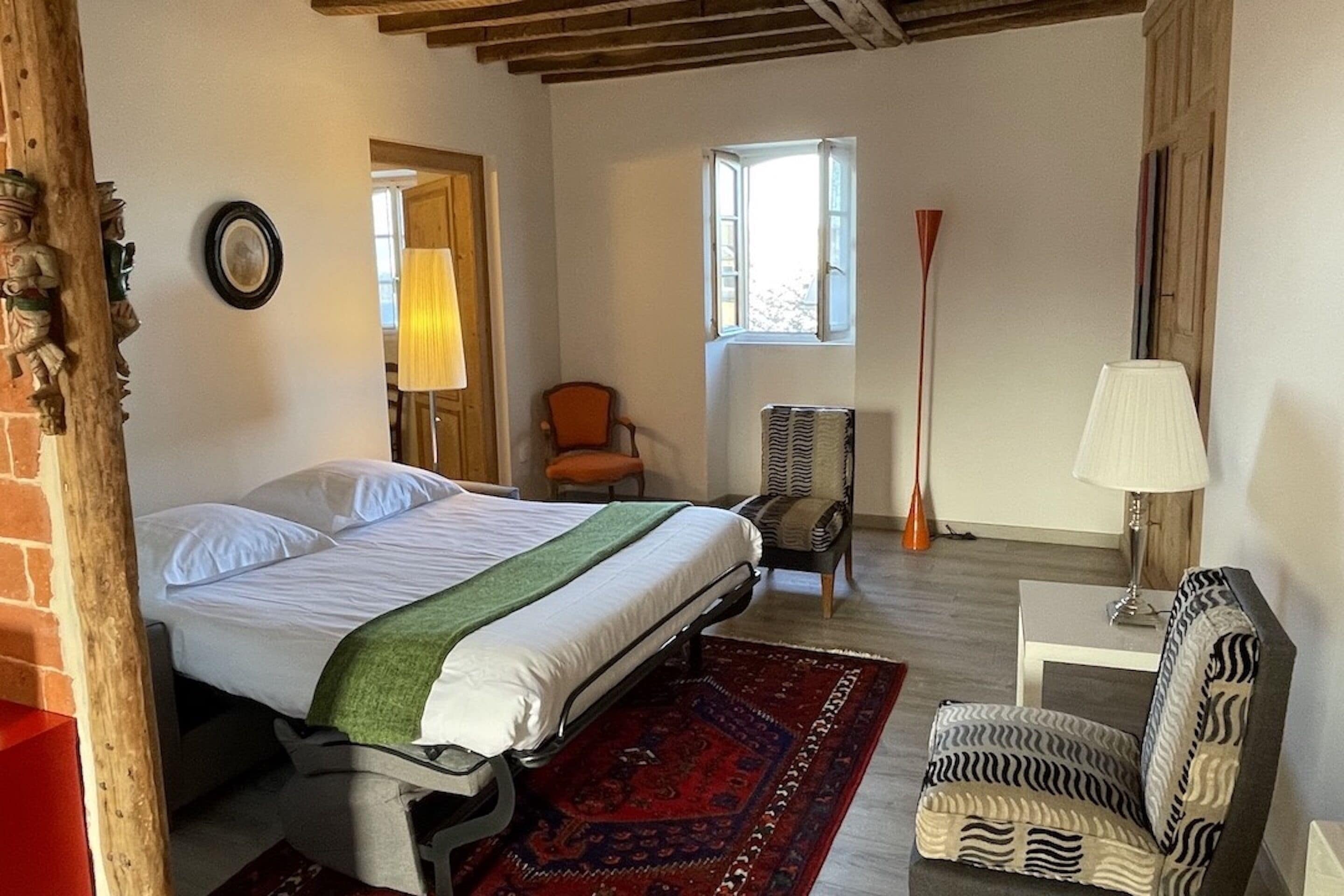 Un dormitorio con cama, una silla, una lámpara y ventana.