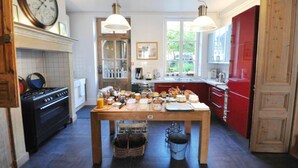 A kitchen with a stove, oven, and a table with food items. - Le Jardin Découverte (Conches-en-Ouche)