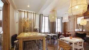 A cozy dining area with wooden tables and chairs, a large vase with dried plants, and hanging light fixtures. - Le Jardin Découverte (Conches-en-Ouche)