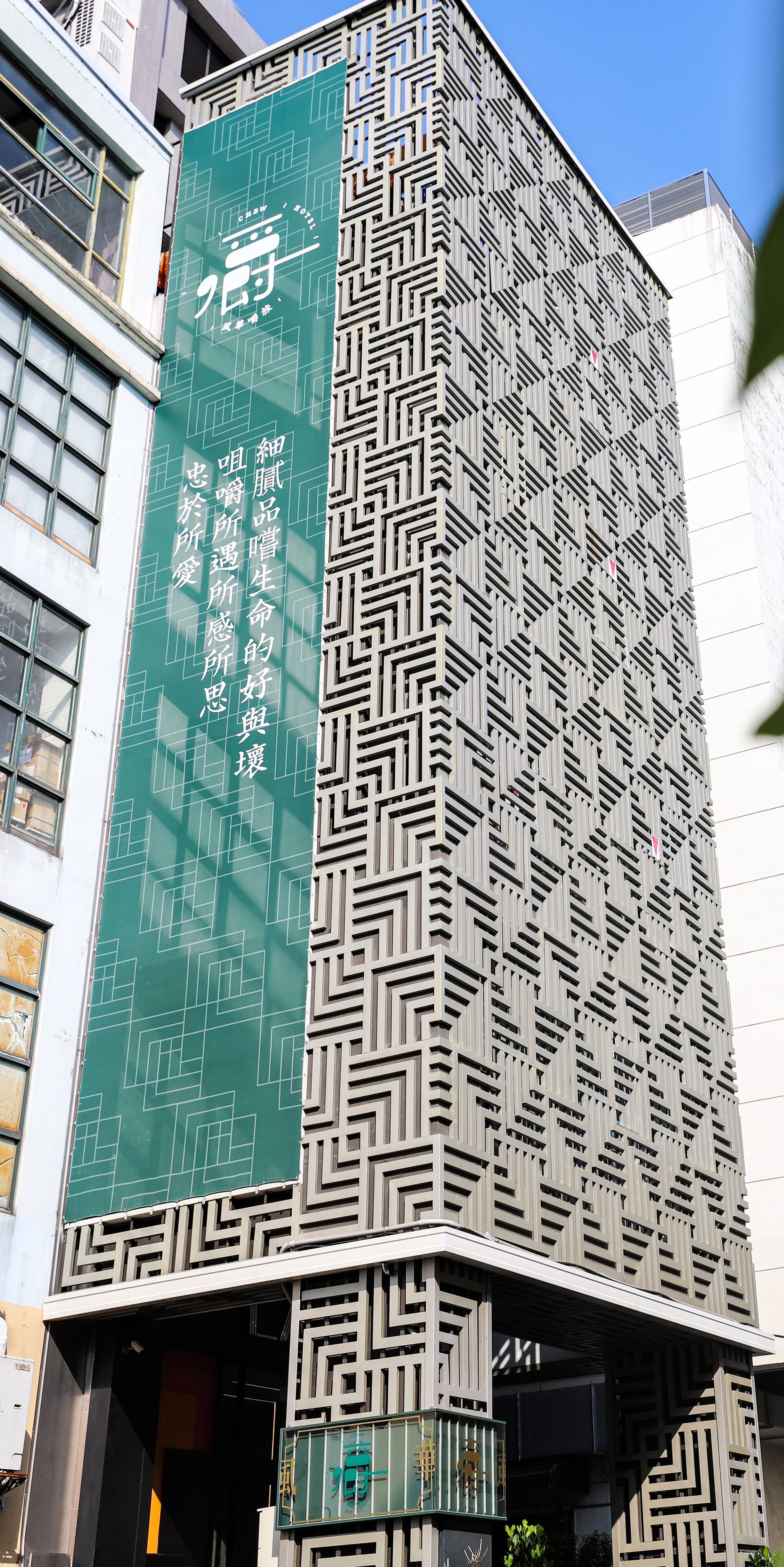 A modern building with a geometric facade and a prominent green vertical banner with text.